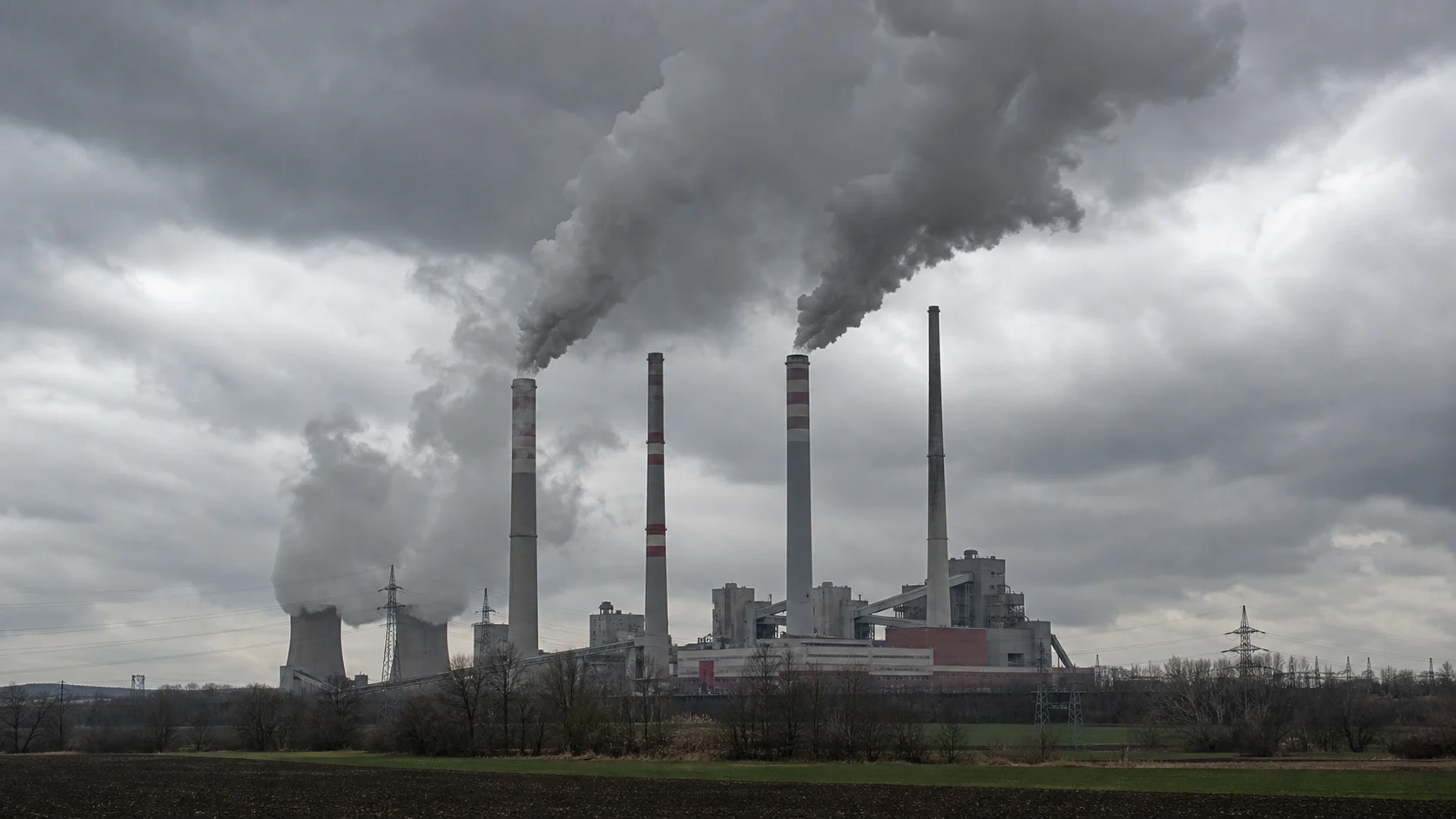 Symbolbild: Rauchende Industrieschlote unter grauem Himmel