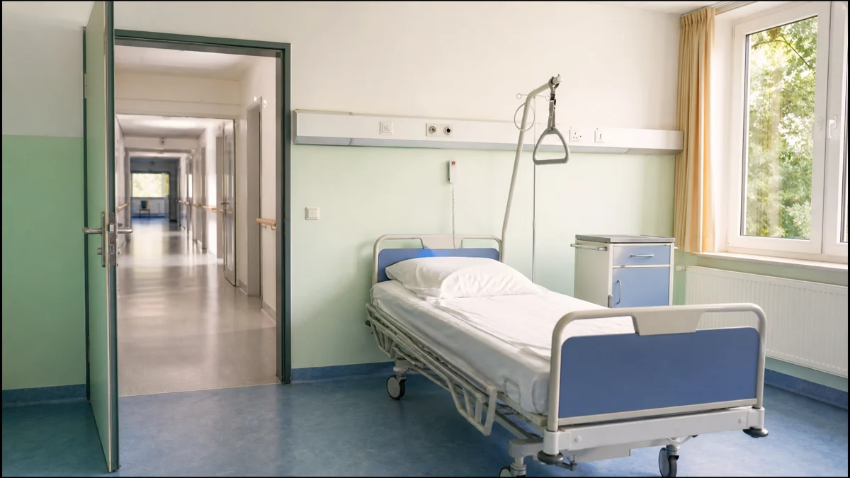 Leeres Pflegezimmer mit Krankenhausbett und Blick in einen verlassenen Flur
