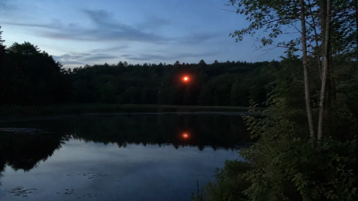 Symbolbild einer roten leuchtenden Kugel über einem abgelegenen Teich in der Dämmerung
