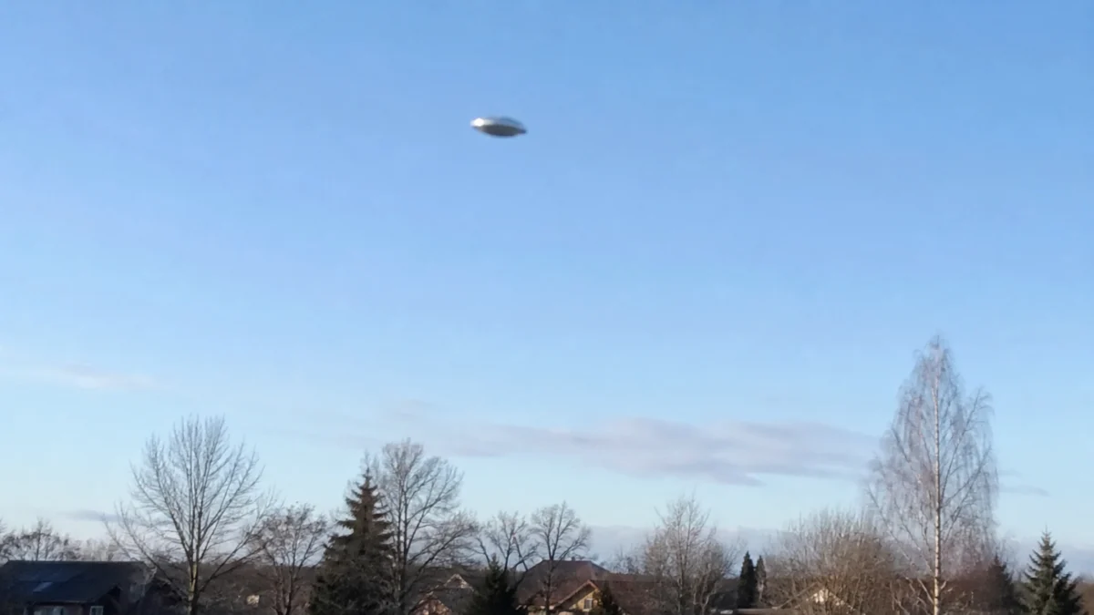 Unscharfes scheibenförmiges Flugobjekt am hellen Himmel über einer Wohnsiedlung