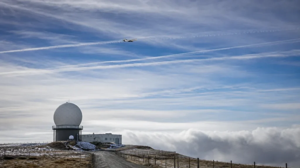 Atmosphärisches Forschungsflugzeug über einer Wetterradarstation und langlebigen Kondensstreifen