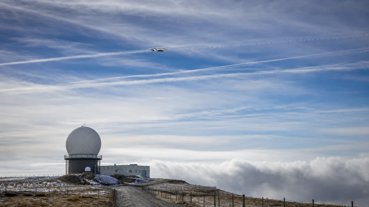 Atmosphärisches Forschungsflugzeug über einer Wetterradarstation und langlebigen Kondensstreifen