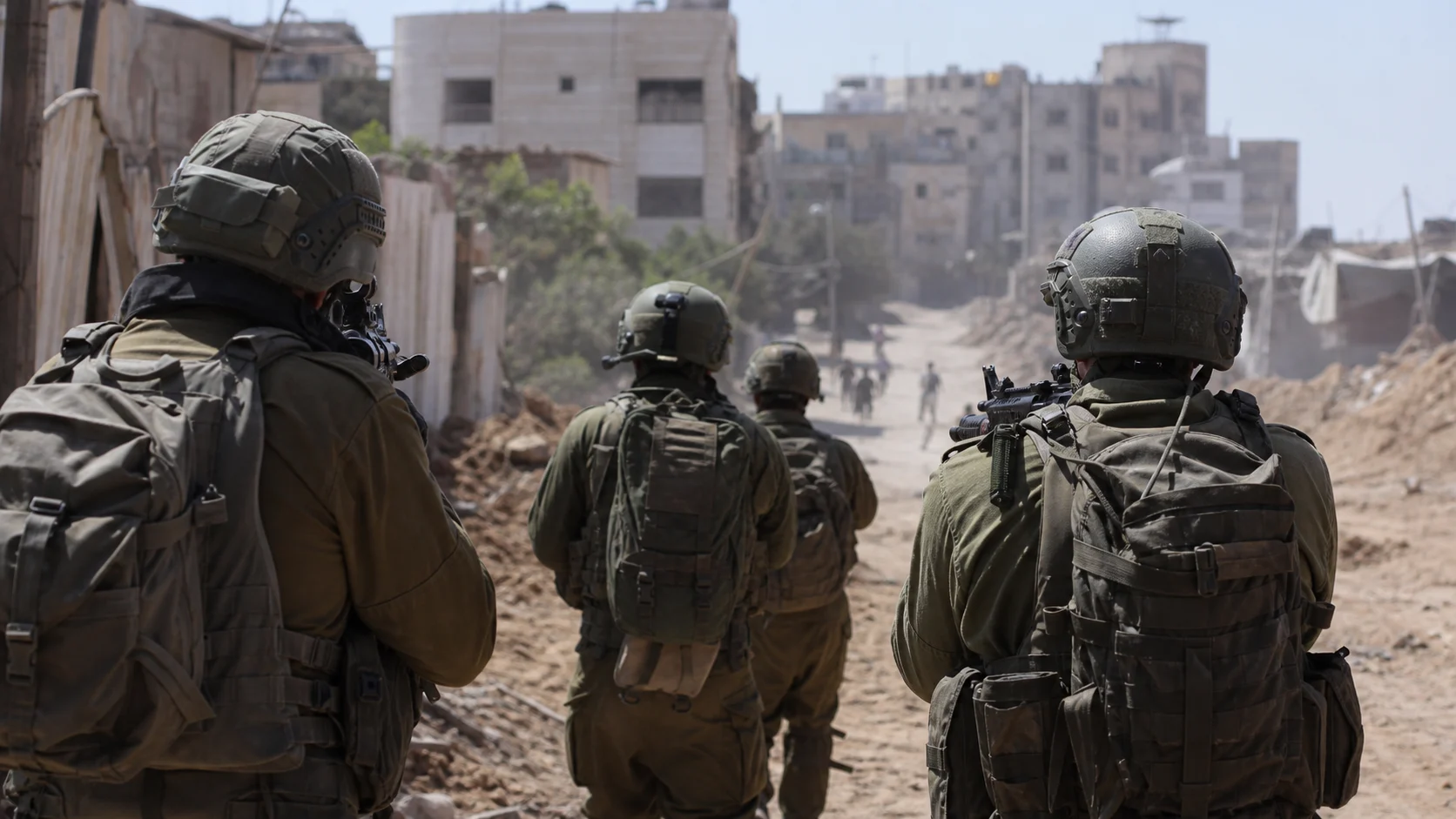 Israelische Soldaten von hinten mit Gewehren im Anschlag und undeutlichen Menschen im Hintergrund