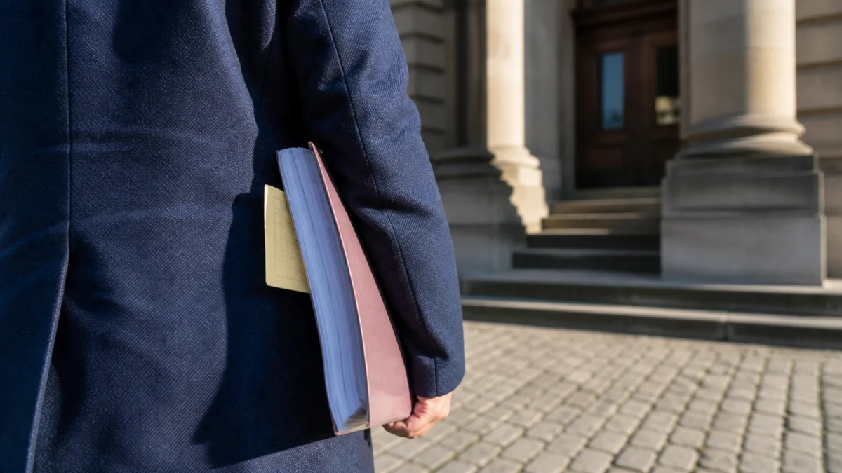Person mit Verfahrensakte vor einem Gerichtsgebäude