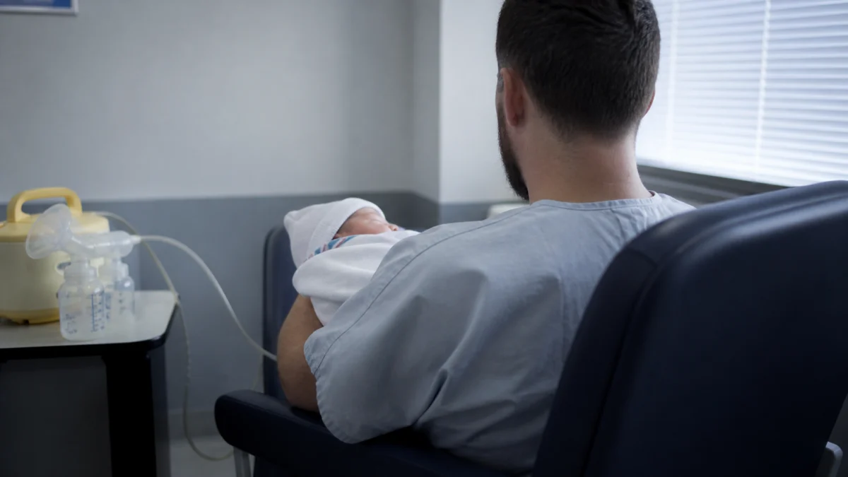 Biologischer Mann hält in einer Klinik ein Neugeborenes neben einer Milchpumpe