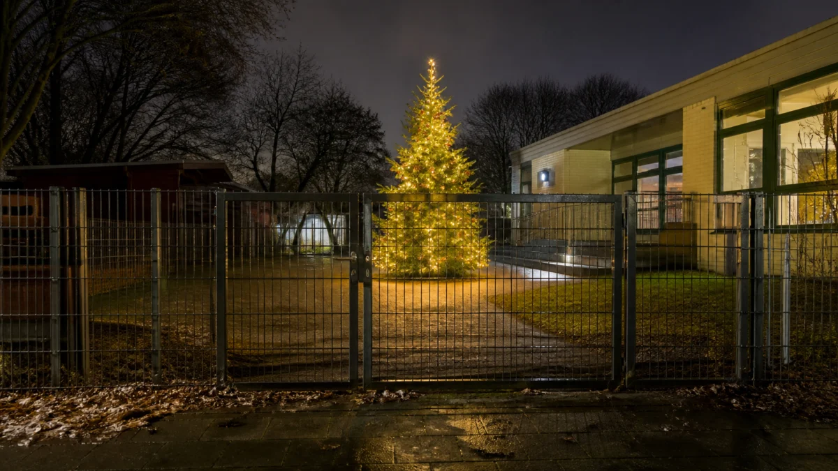 Beleuchteter Weihnachtsbaum hinter dem verschlossenen Tor einer Kindertagesstätte.